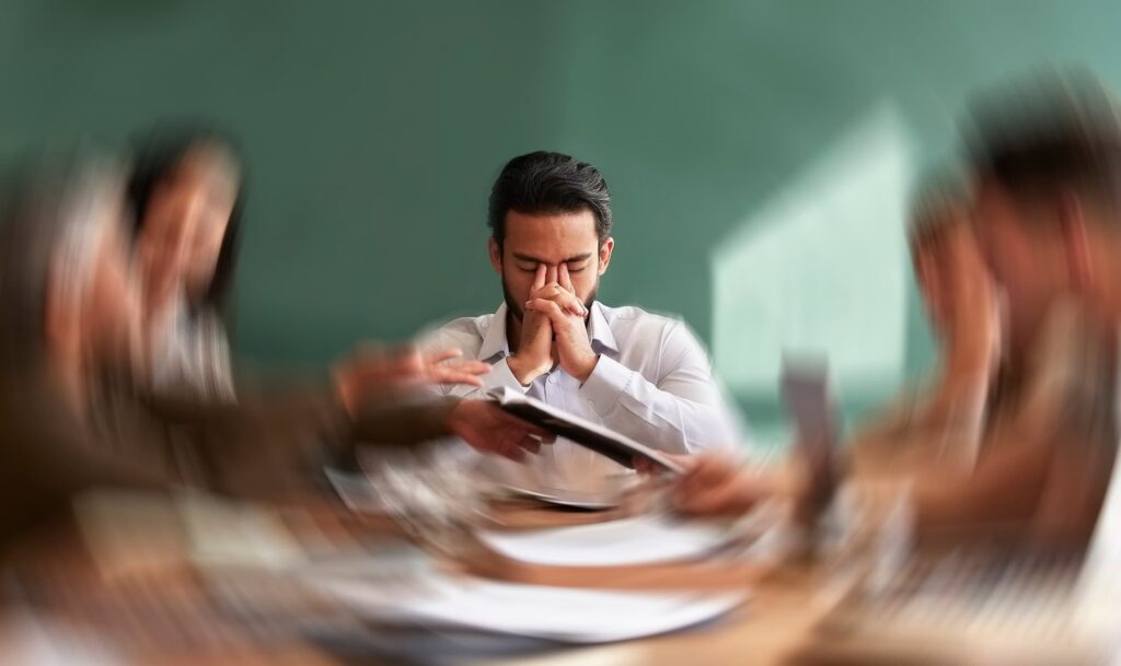 A man having an anxiety attack sitting at a table holding his face while the room spins