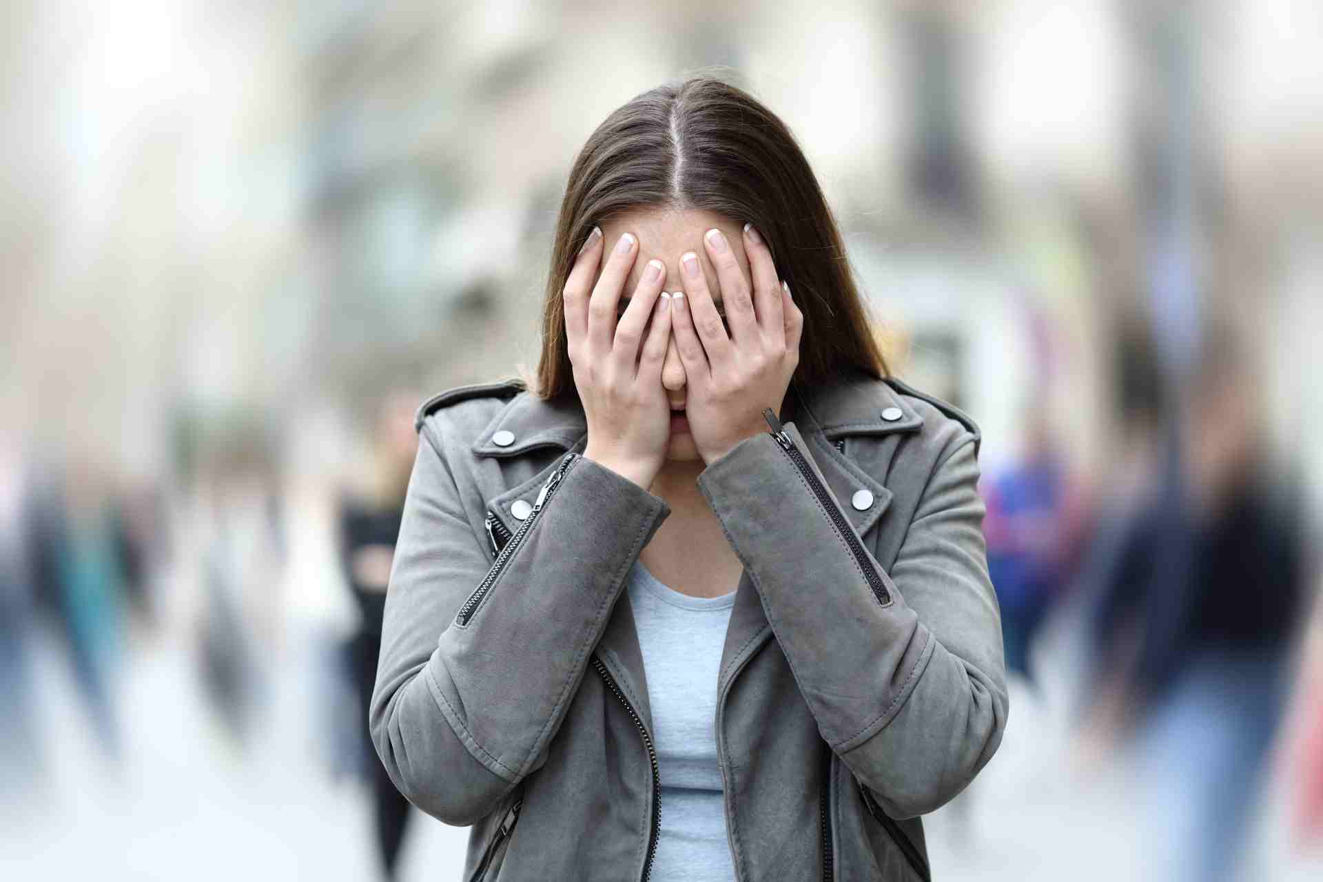 Woman covering her face while experiencing anxiety in a crowded public setting