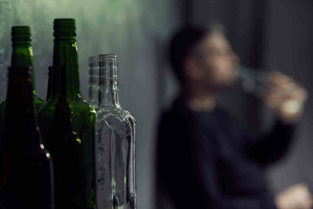 Blurred man drinking alcohol in the background with empty liquor bottles in the foreground